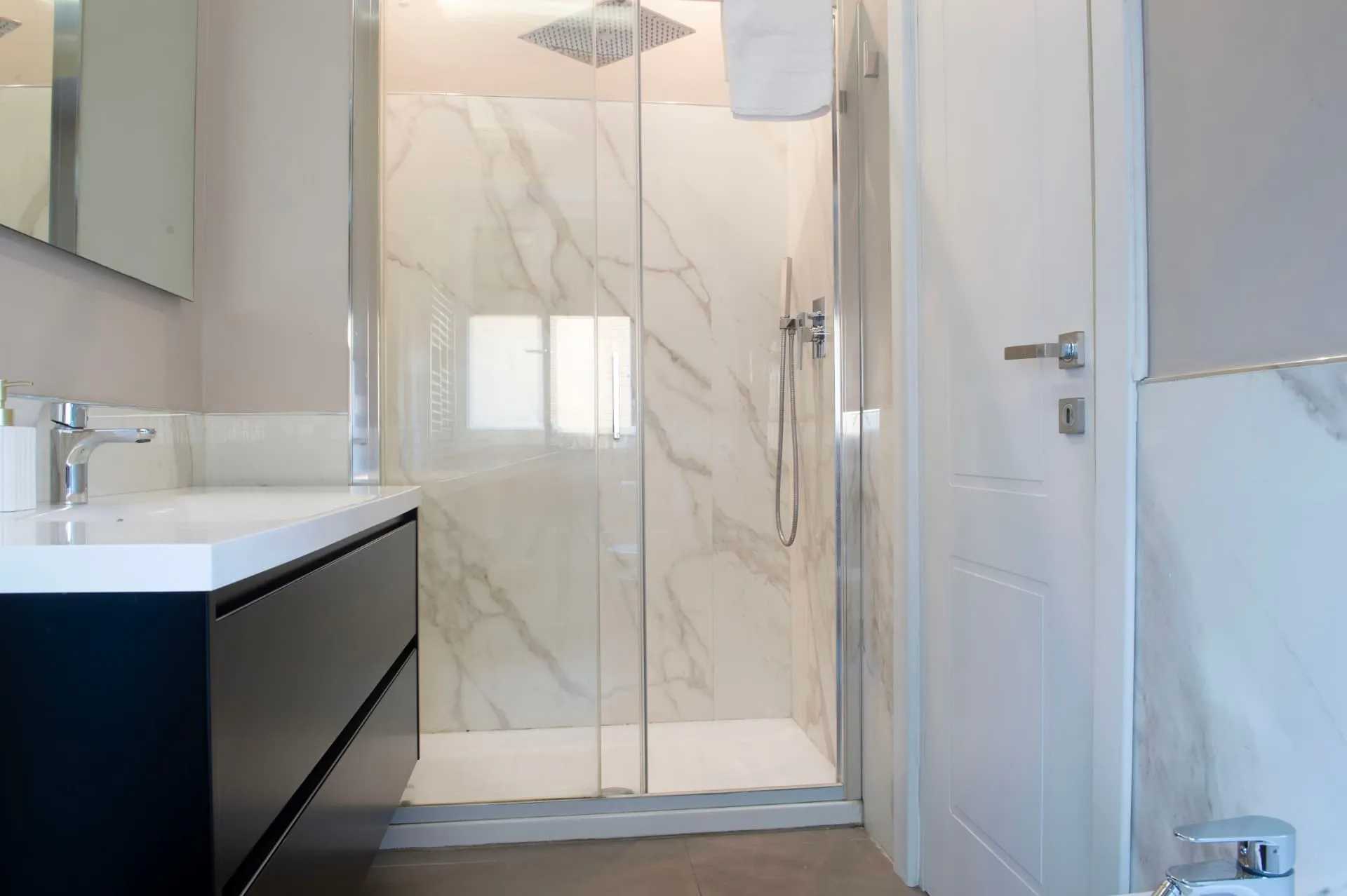 Bagno con doccia in marmo bianco e mobile lavabo nero
